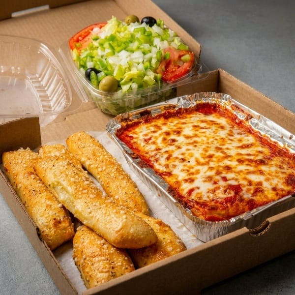 Baked lasagna, garlic breadsticks, and a side salad in a takeout box.