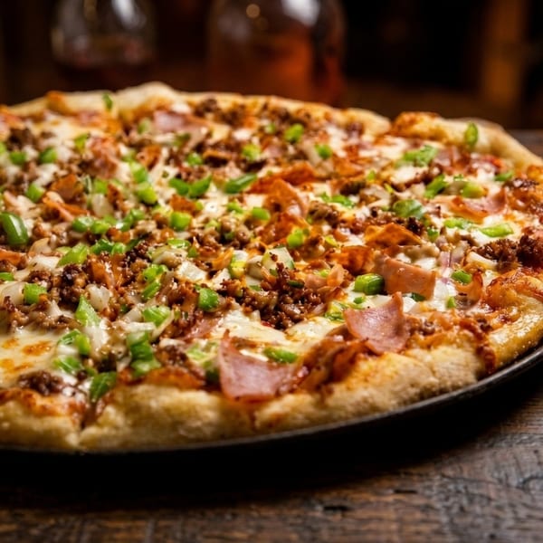 Close-up of a whole pizza topped with ground meat, ham, green peppers, and onions.